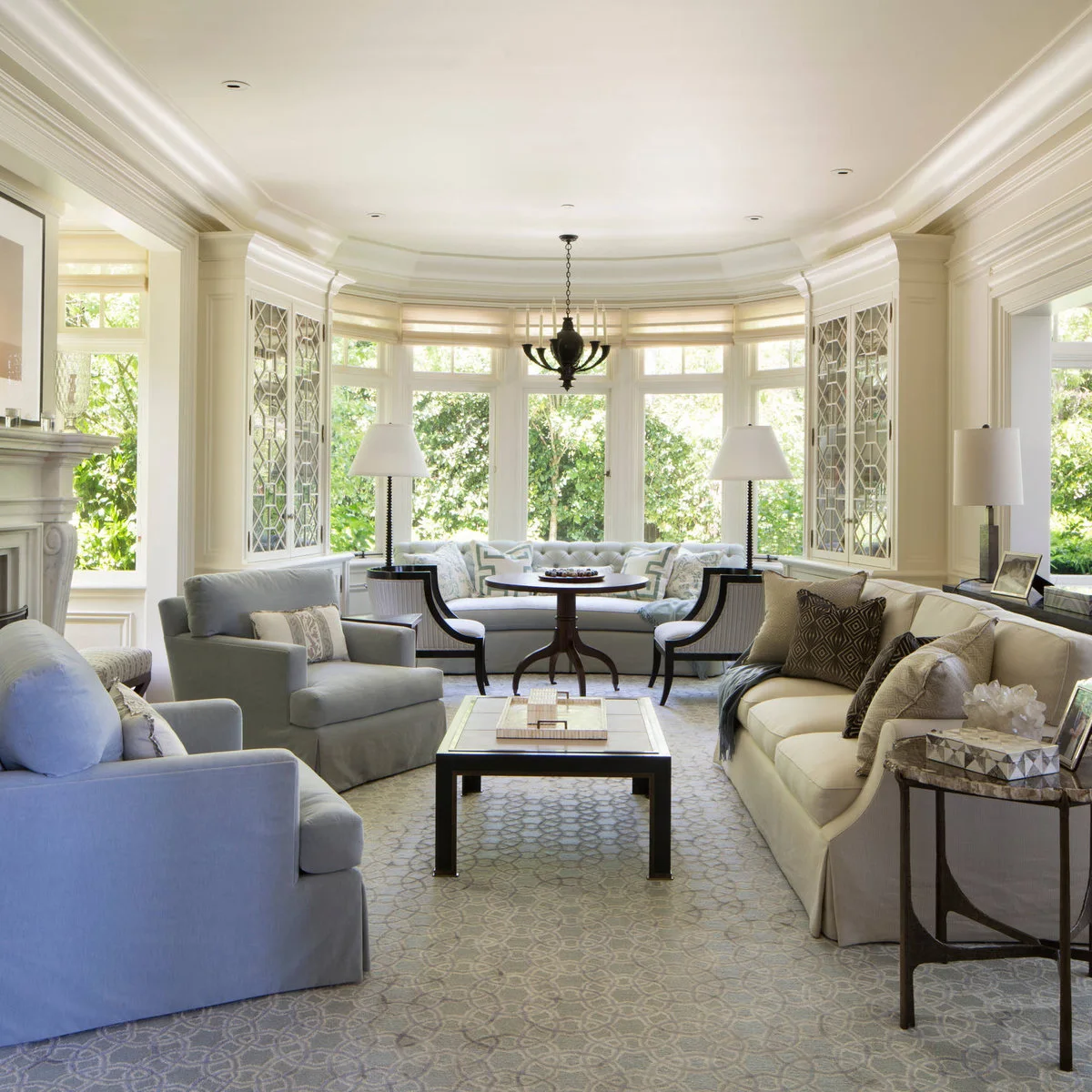 Long cream living room with blue armchairs, a pale sofa and a round table beside a curved window seat