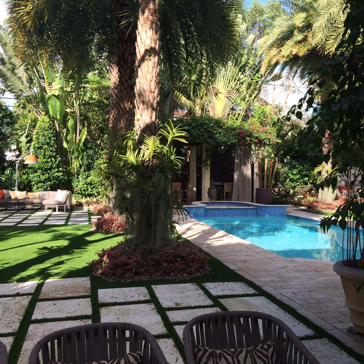 A Coral Gables courtyard with a pool, pale paving with green joints, seating and palms growing in distinct planted circles.