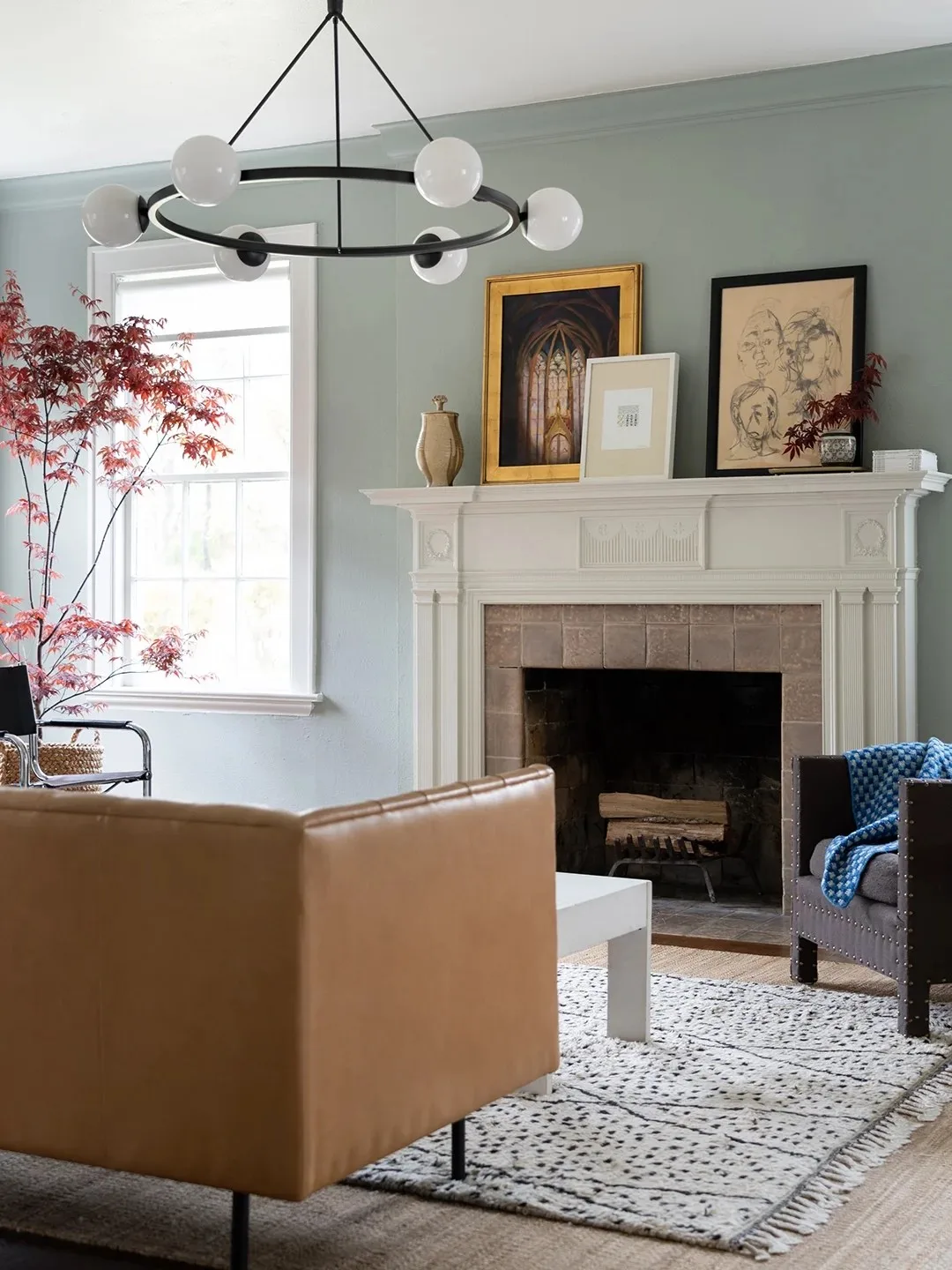 The back of a tan leather sofa faces a pale fireplace in a blue-gray room with framed artwork
