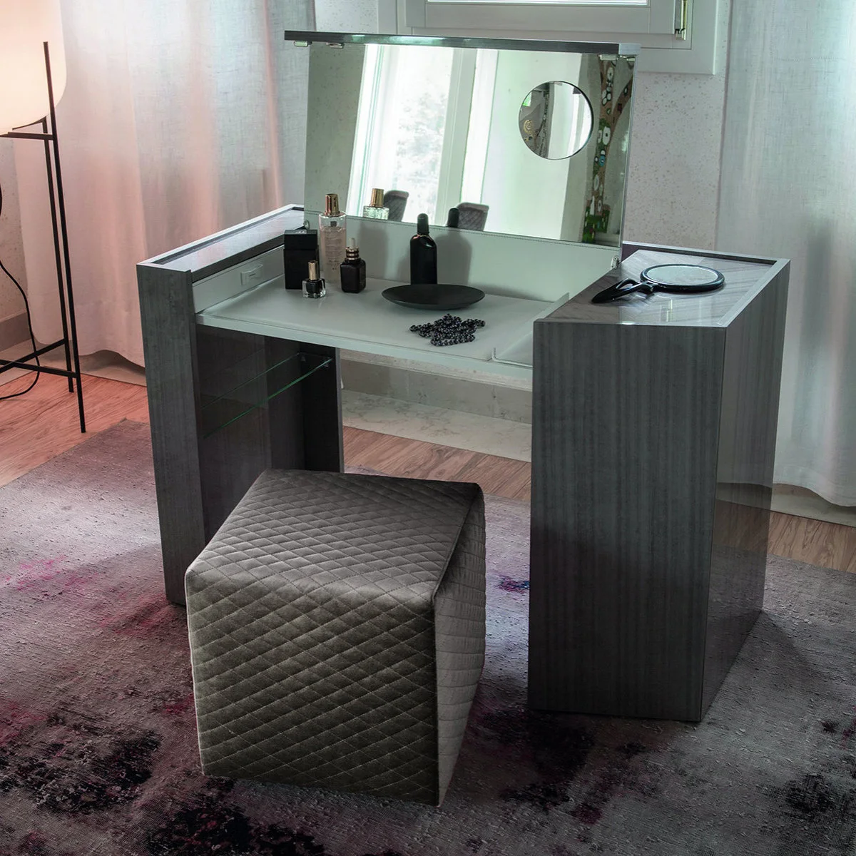 A dark dressing table has an open central mirror lid, side compartments and a quilted stool