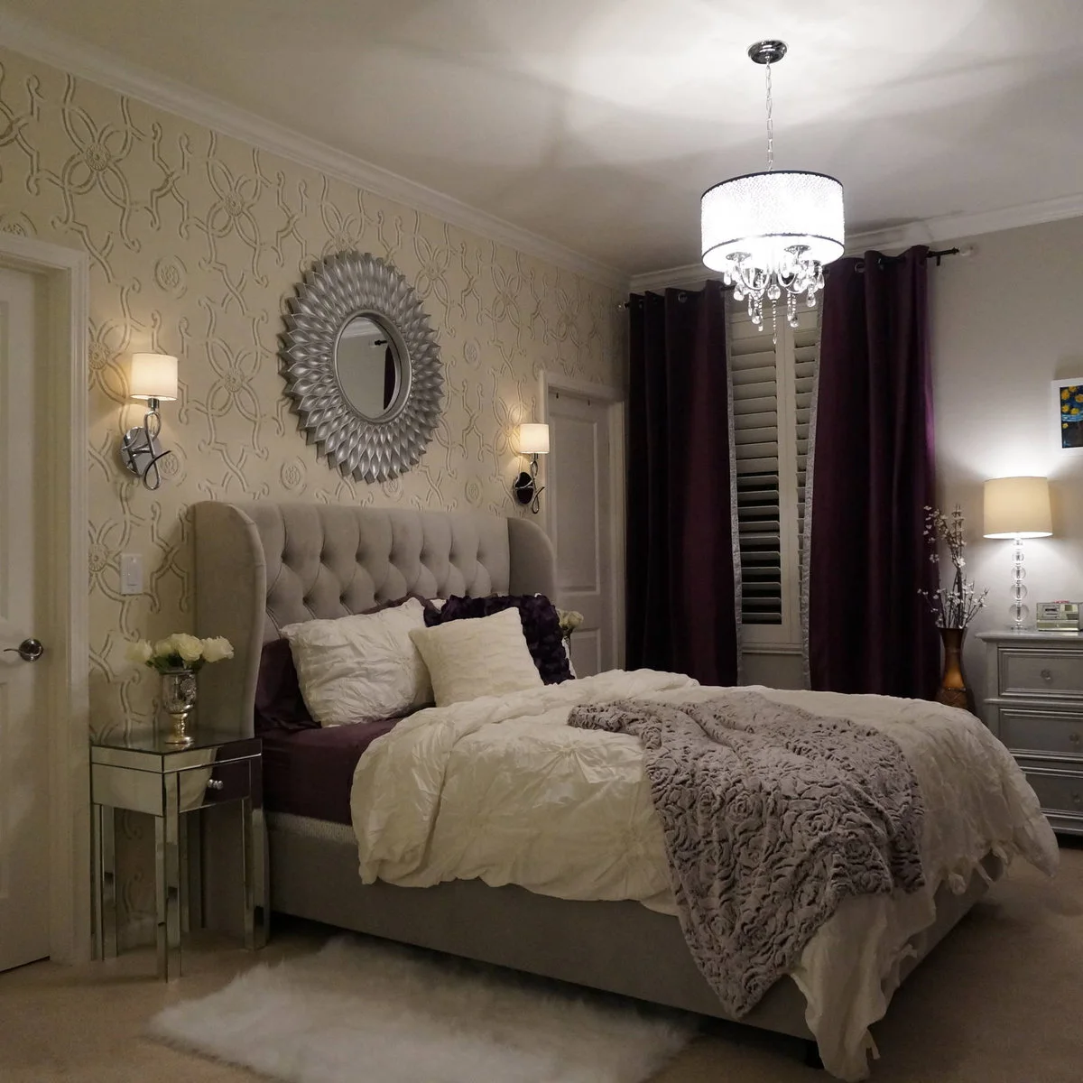 Teen bedroom with a tufted pale headboard, purple curtains and wall lights against patterned wallpaper