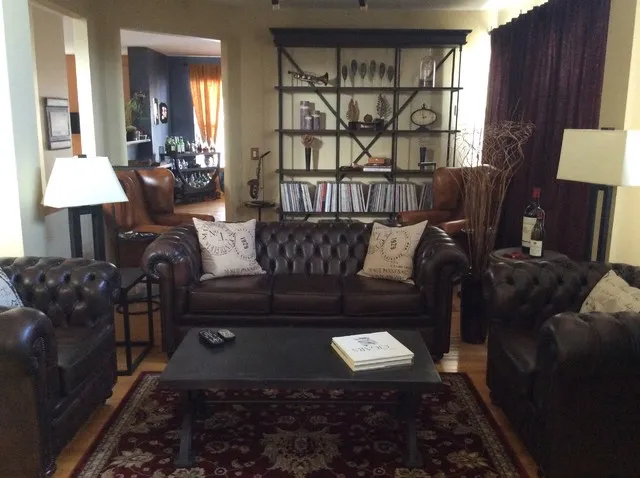 Dark tufted leather sofas surround a low black table with pale cushions and brown chairs behind