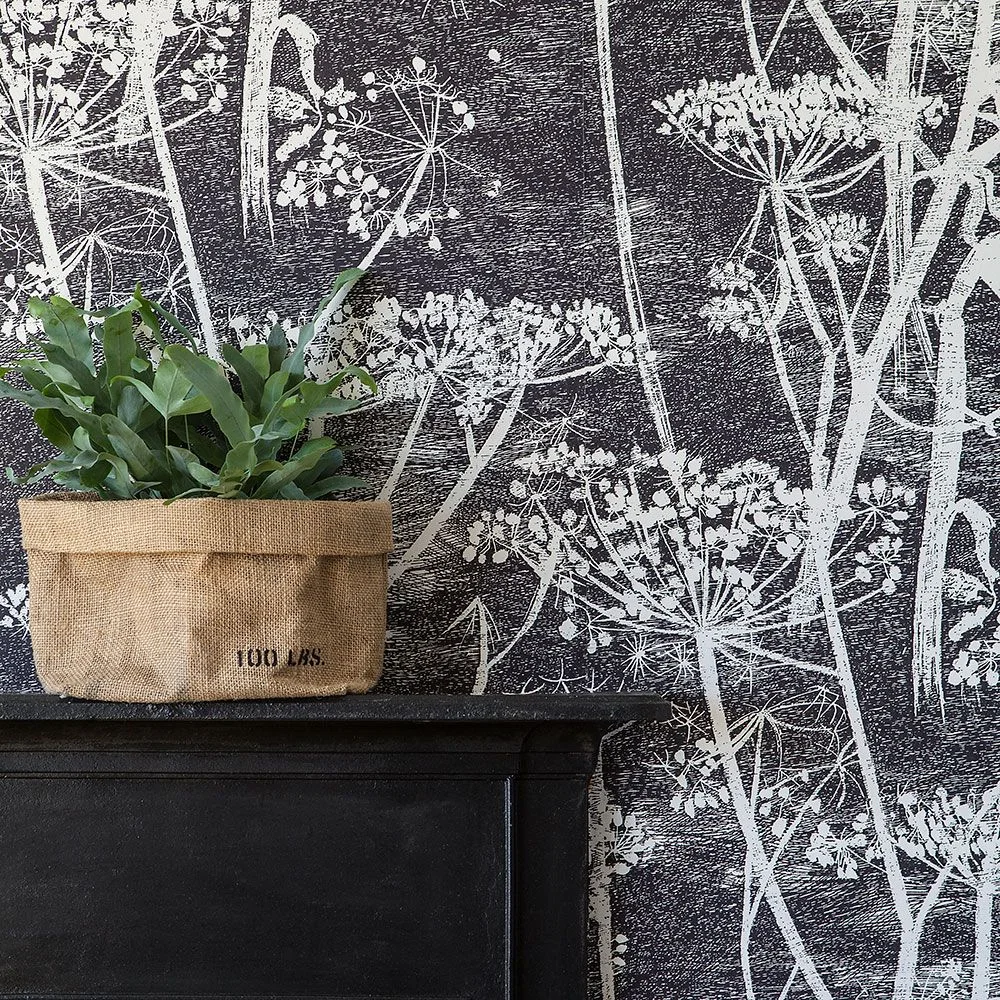White botanical stems cover a charcoal wall above a dark cabinet topped with a leafy plant in a coarse woven container.
