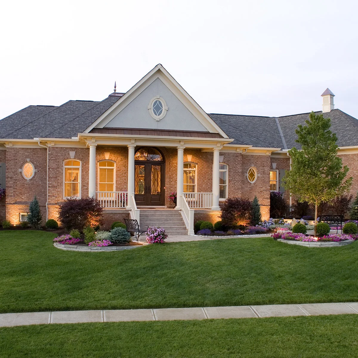 Low pale masonry edges form curved flower beds on either side of a front path and porch steps.