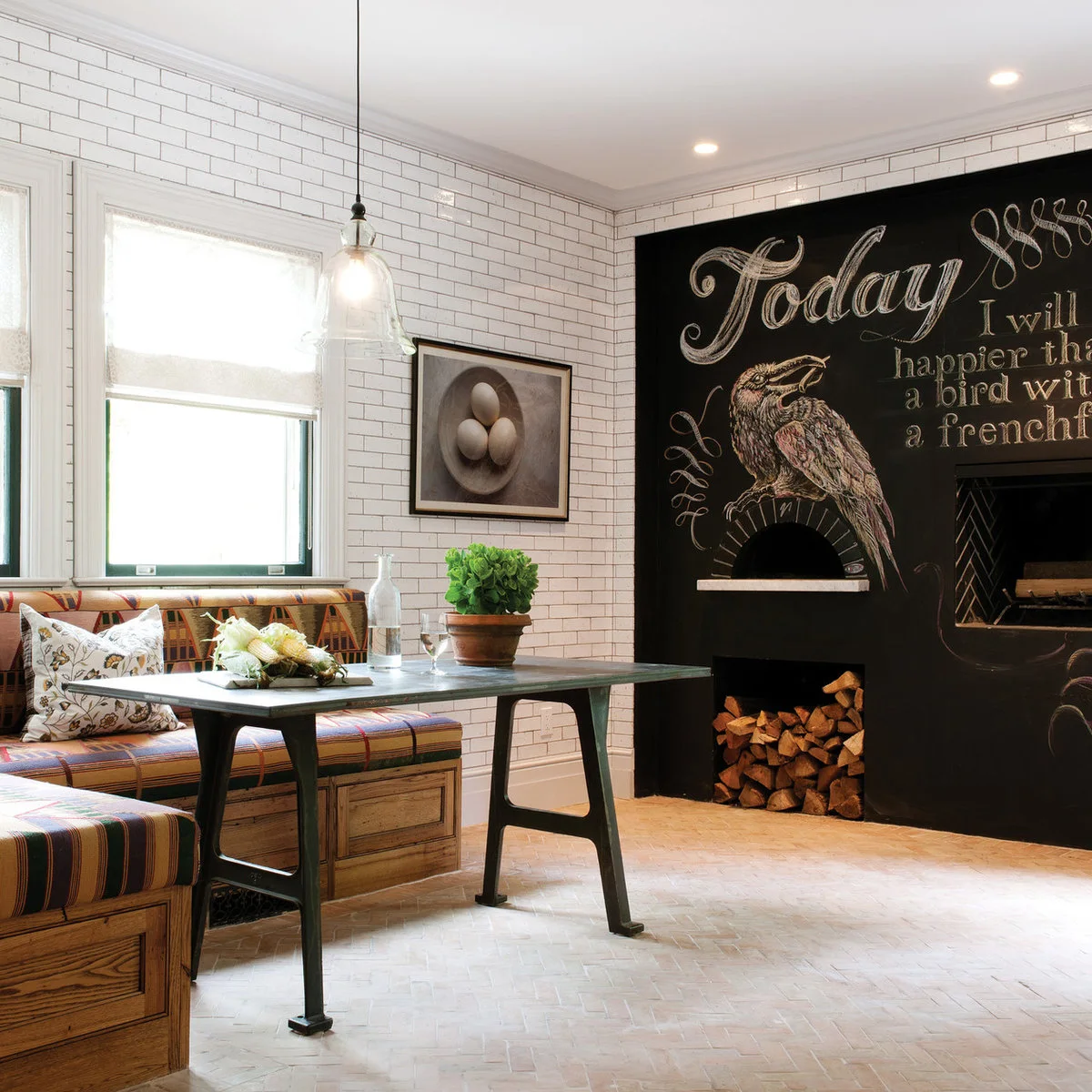 Large black chalkboard surface with a bird drawing beside a tiled kitchen eating nook and wooden banquette.