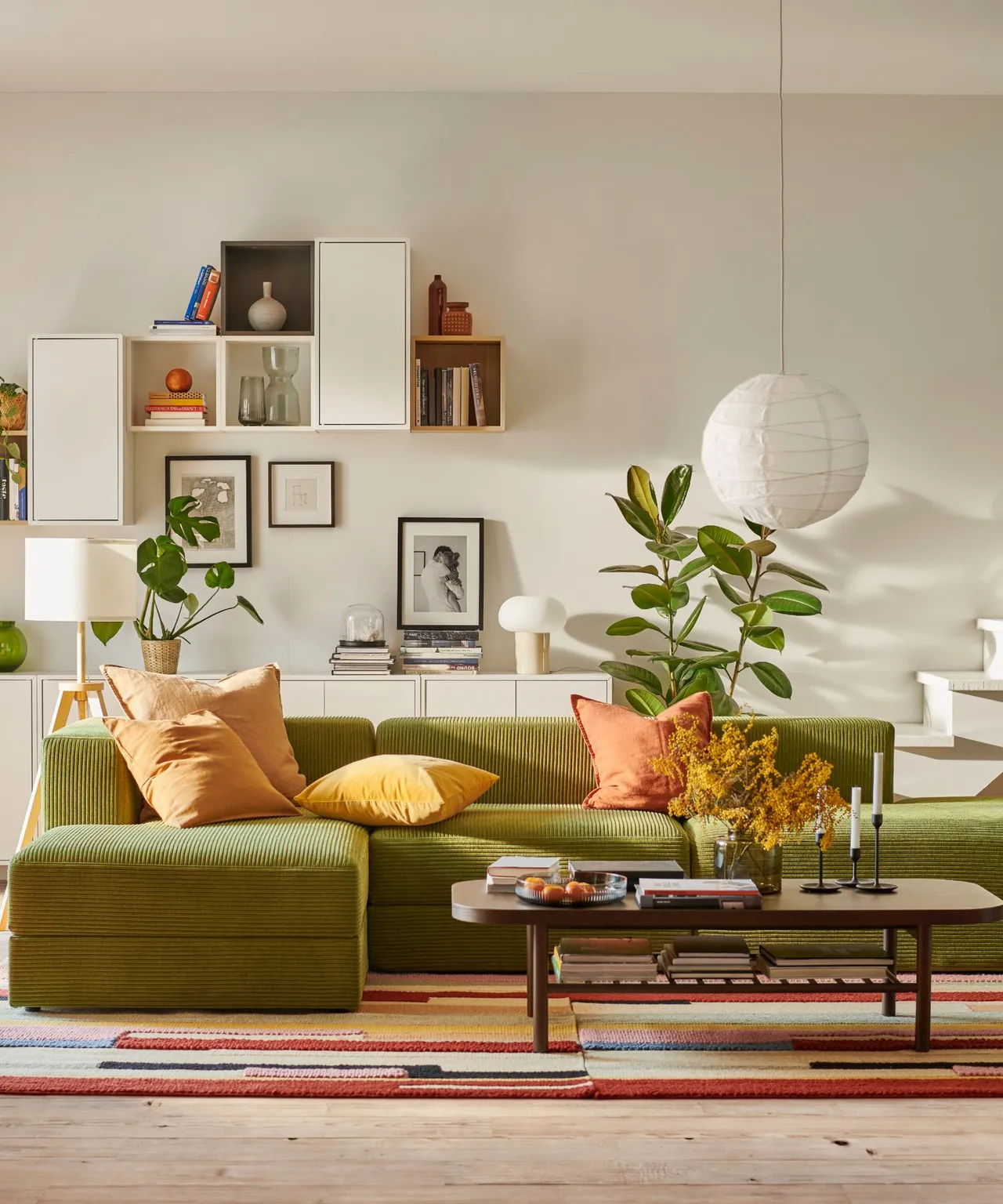 A ribbed olive green sectional sofa sits below open shelves with warm orange and yellow cushions