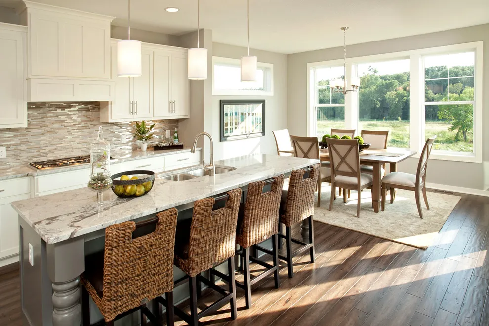 Woven stools line a pale kitchen island opposite cream cabinets and a layered tile backsplash