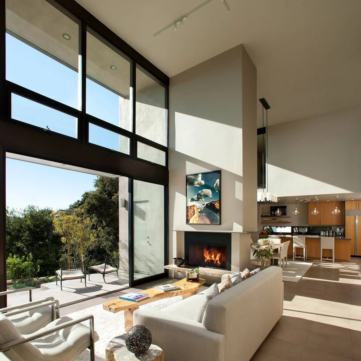 Double-height living area with a white sofa facing a fireplace and an open kitchen behind it