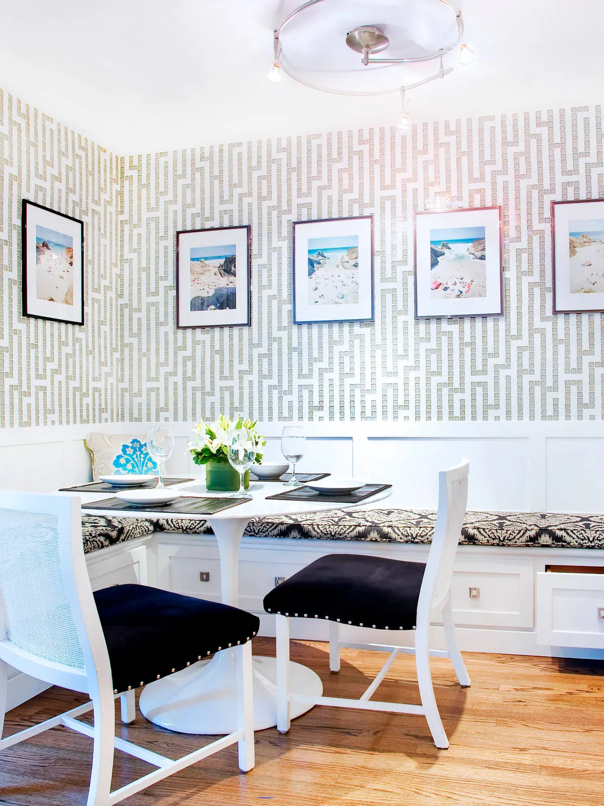 A small geometric wall pattern sits behind a row of framed pictures and white dining chairs.