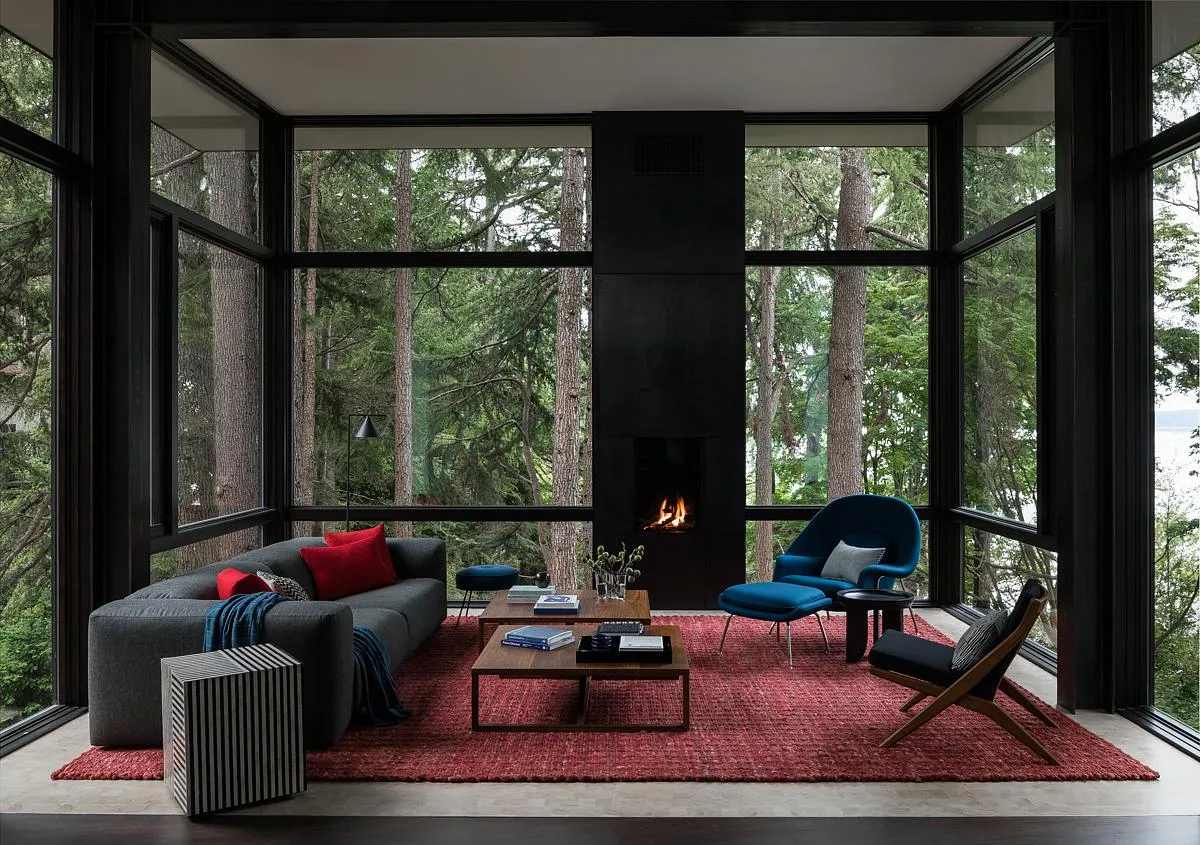 A dark gray sofa sits on a red rug beside a blue chair and black-framed windows