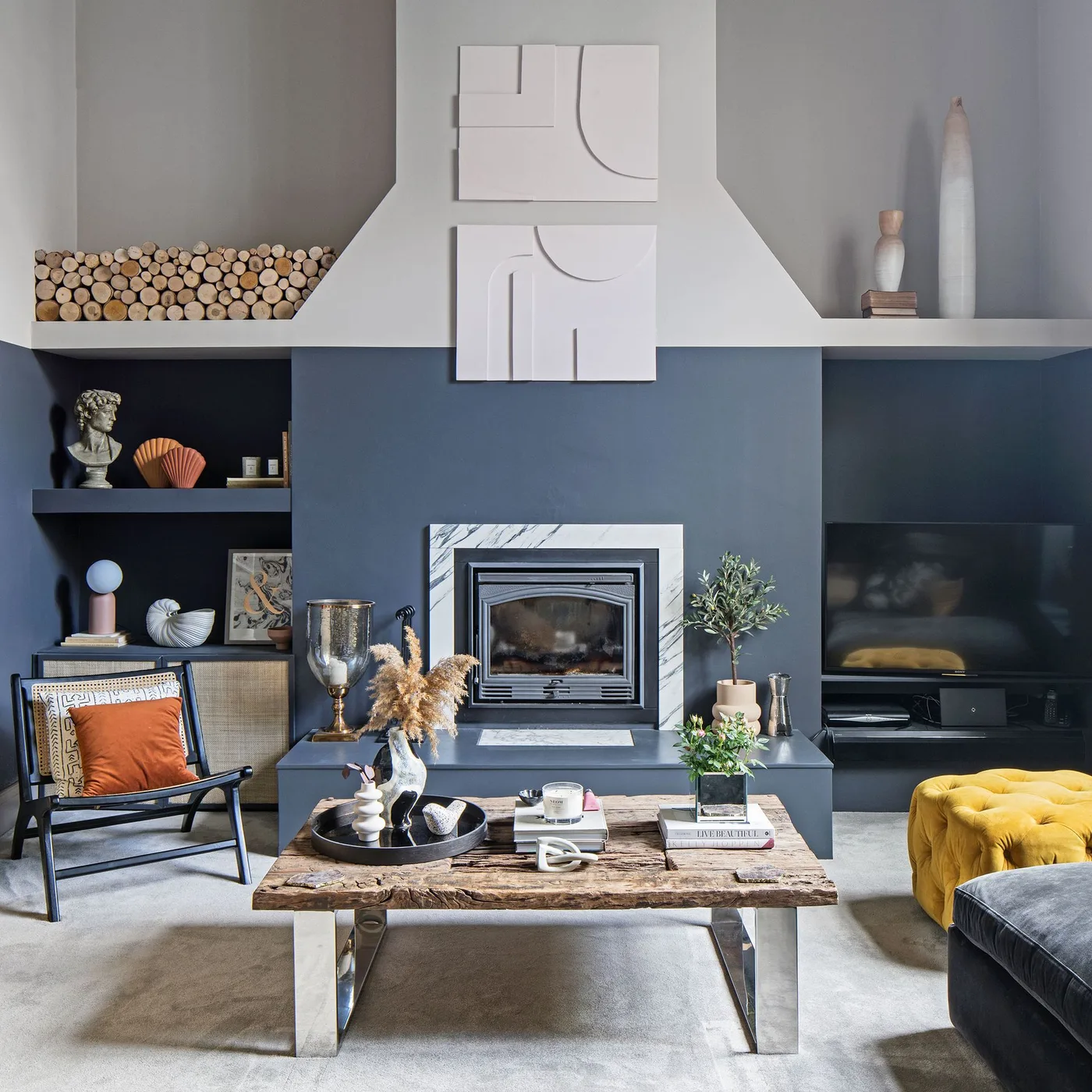 Blue fireplace wall with pale tapered chimney, high display ledge, two relief panels, logs and tall vessels