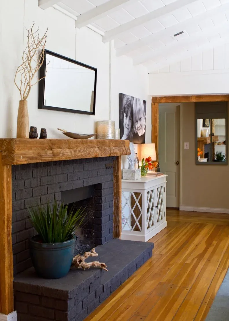 Dark brick fireplace with a thick wooden mantel, black-framed mirror and matching warm doorway trim.