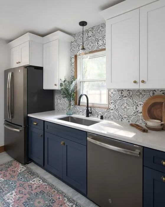 Navy lower cabinets and white upper cupboards surround a sink below fine pale patterned tiles with a dark faucet and small glass pendant
