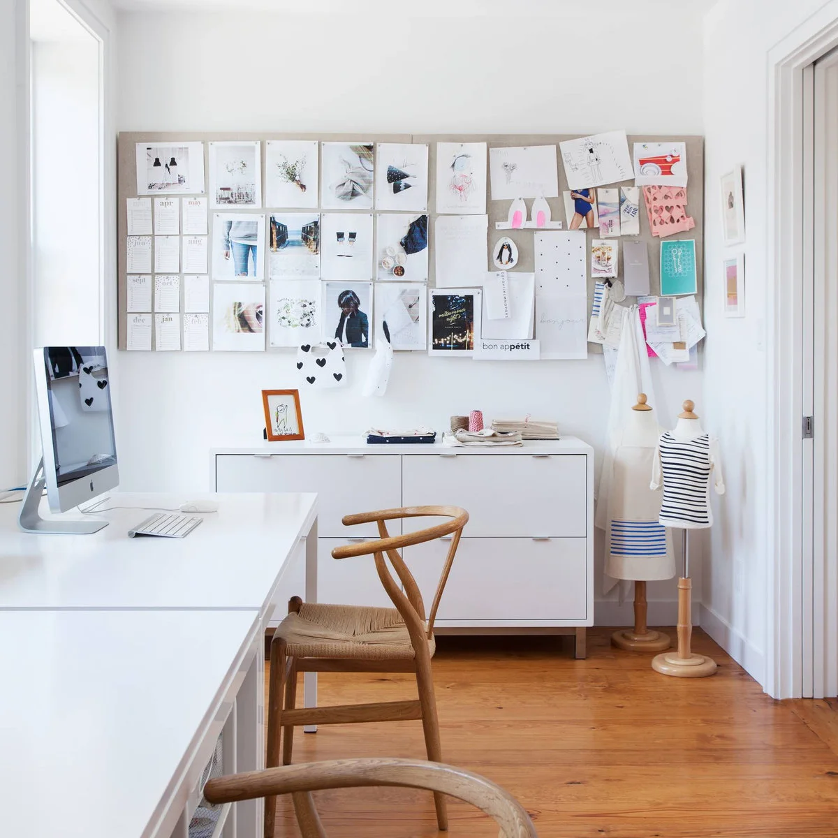 White work surface with wood chairs beside a low white storage cabinet and a large reference board