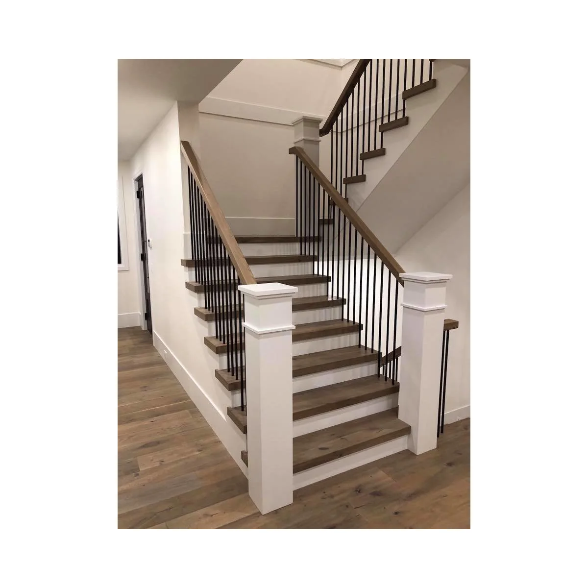 Turning staircase with white square newel posts, wood treads and slim black vertical balusters
