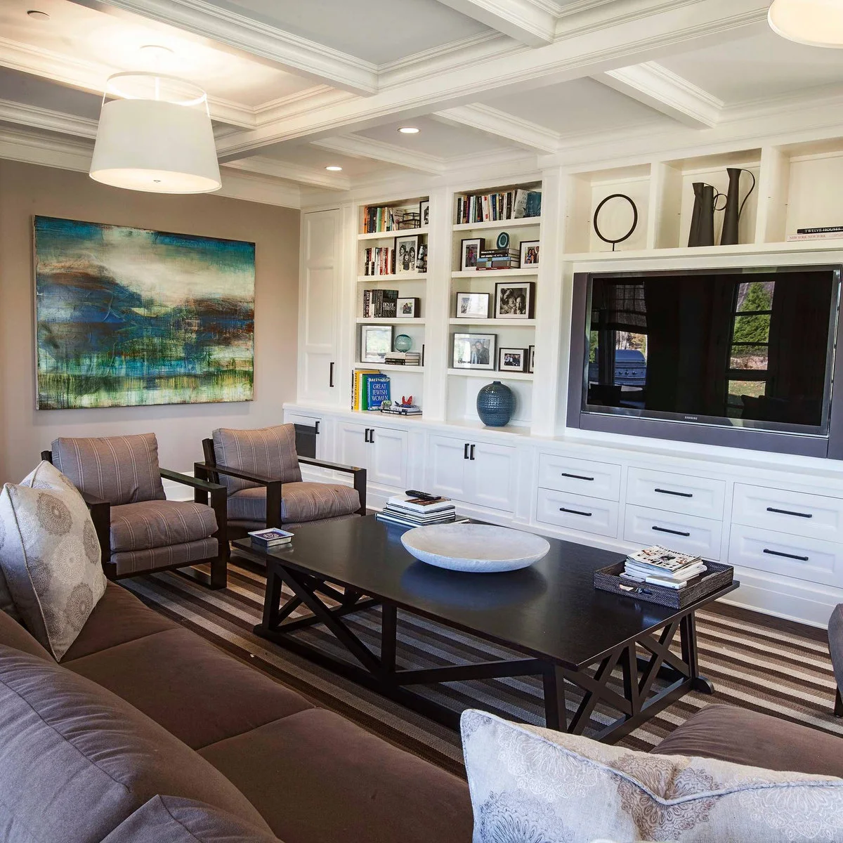 Three white niches holding dark sculptural objects and books above a television within a large built-in wall.