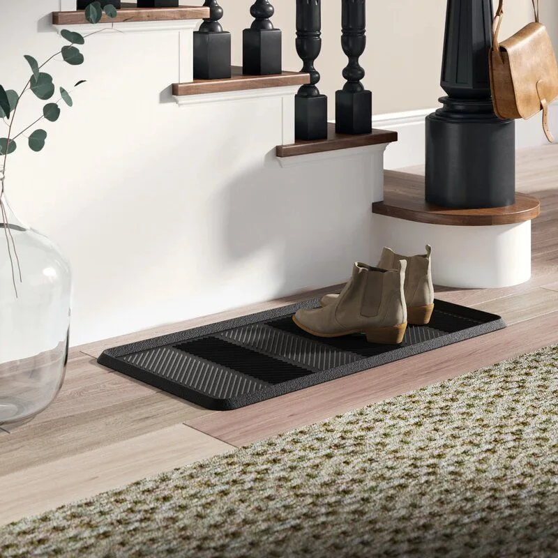 Entry beside a staircase with a long dark ridged boot tray, two ankle boots, pale wood floor and nearby textured rug