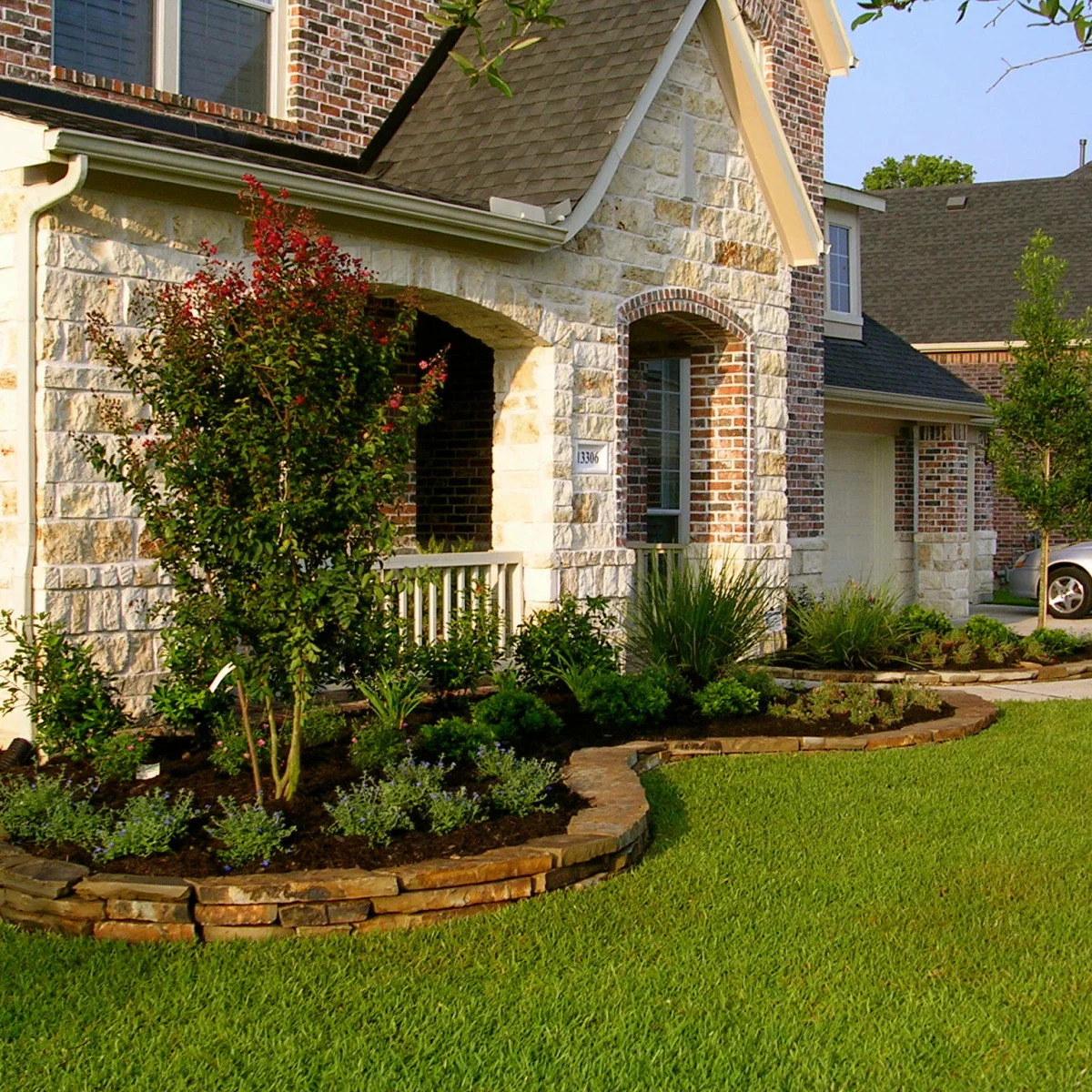 A stone-and-brick front porch with rounded shrubs, upright grasslike foliage and a curved stone-edged bed.