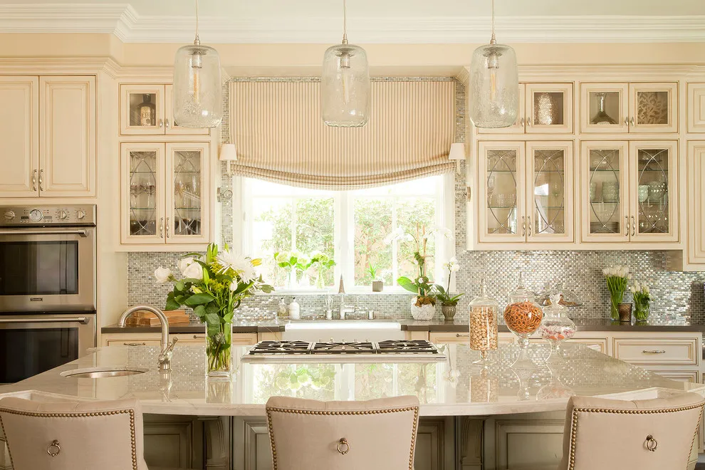 Cream-beige cabinets with glass upper doors frame a window and a large island