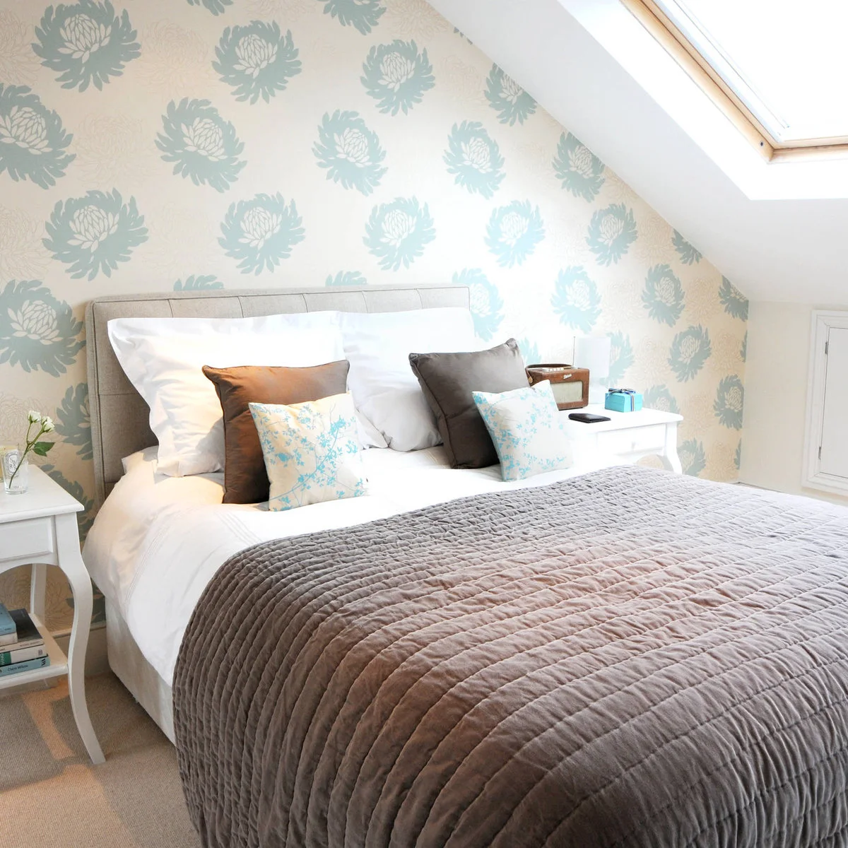 White curved-leg bedside table with lower shelf against pale blue floral wallpaper