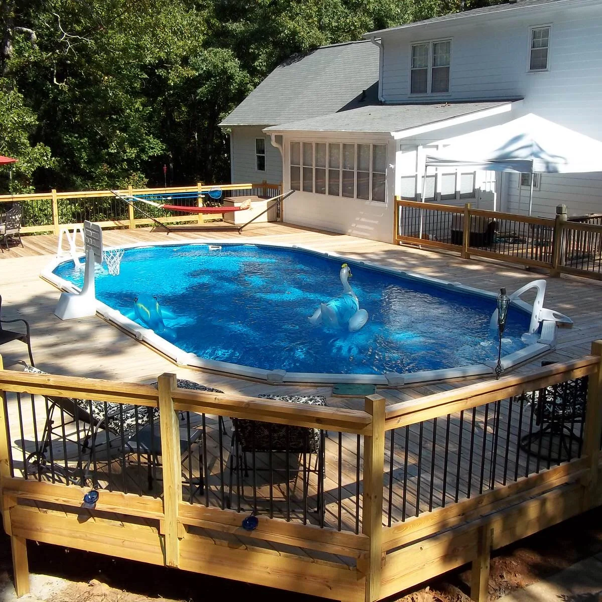 Oval above-ground pool surrounded by wood decking with a hammock near the house and a separate shaded seating area.