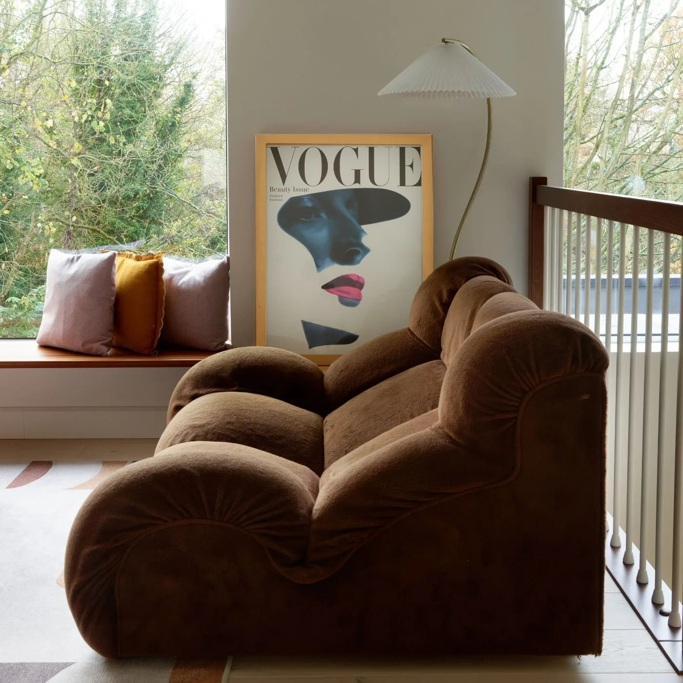 Sculptural brown sofa near large windows with a curved floor lamp and a simple window bench