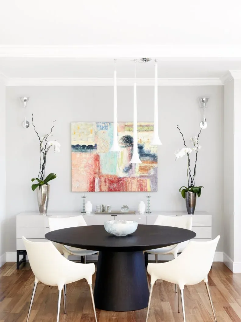 White suspended dining cabinet beneath abstract artwork behind a black round table and white chairs