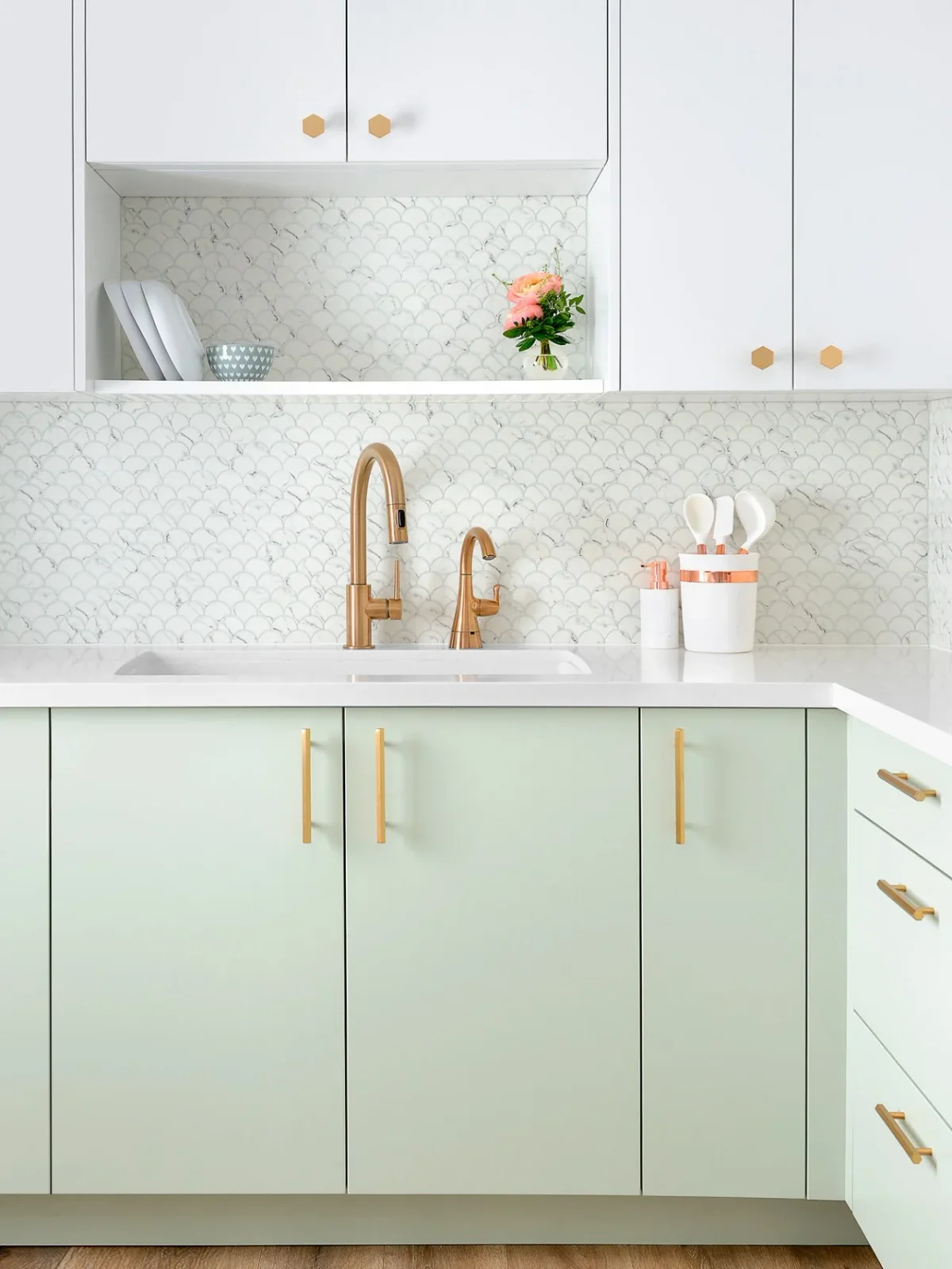Mint green sink cabinets sit beneath white uppers and a scalloped pale backsplash, with gold-colored pulls, knobs and taps.