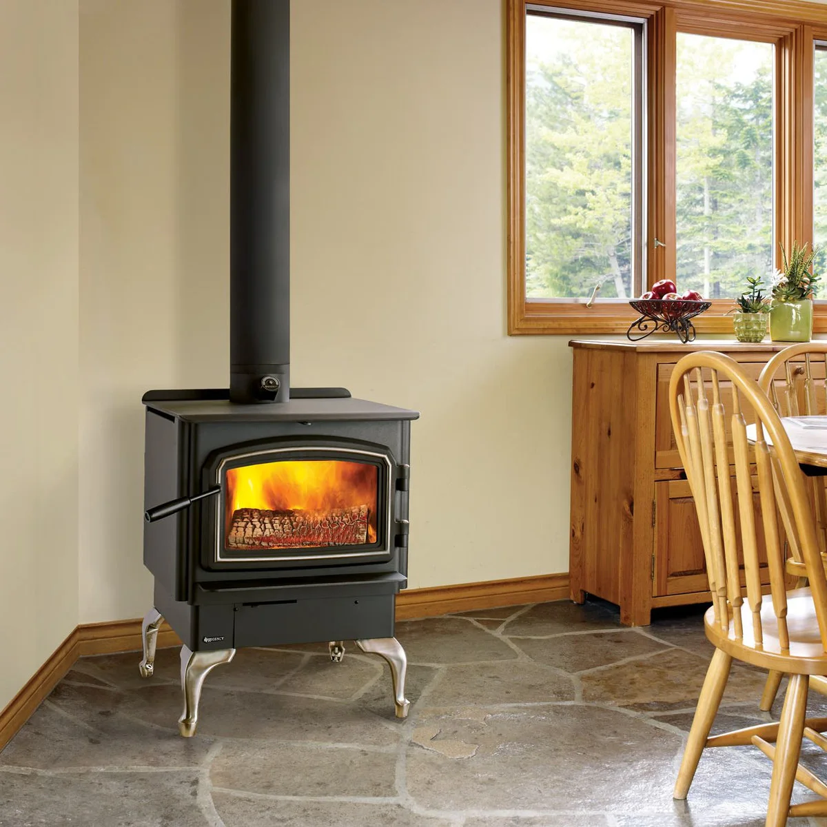 A black stove with bright metal legs stands on an irregular stone-patterned floor beside timber dining chairs and a low cabinet.