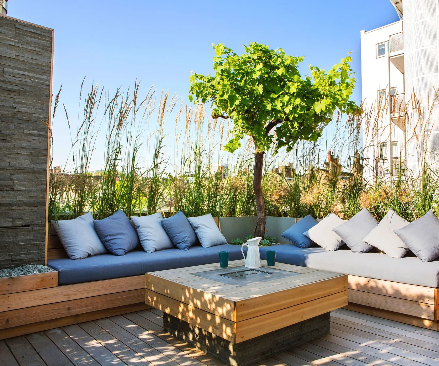 Tall fine grasses rise behind blue-cushioned corner seating on a timber balcony