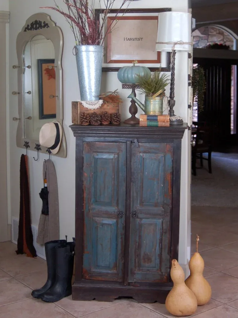 Blue distressed cupboard beside shaped wall mirror with hooks, hanging hat and boots