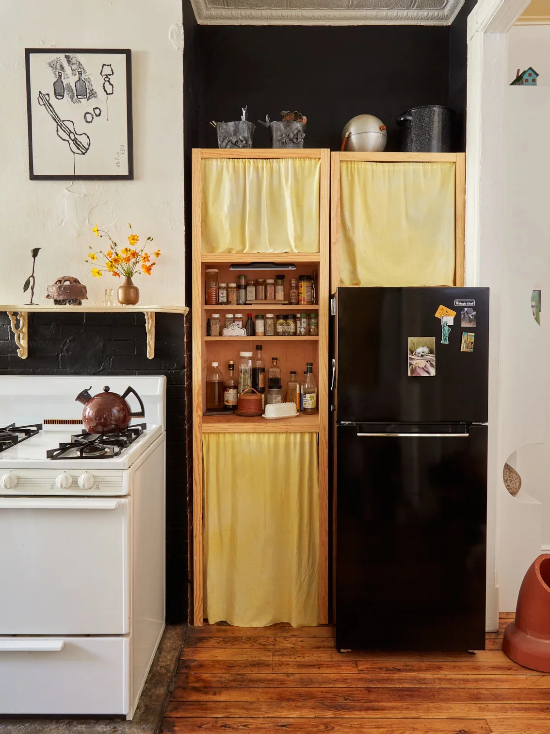 Tall wood kitchen storage with yellow fabric panels and larger dark containers arranged above it against a black recess.