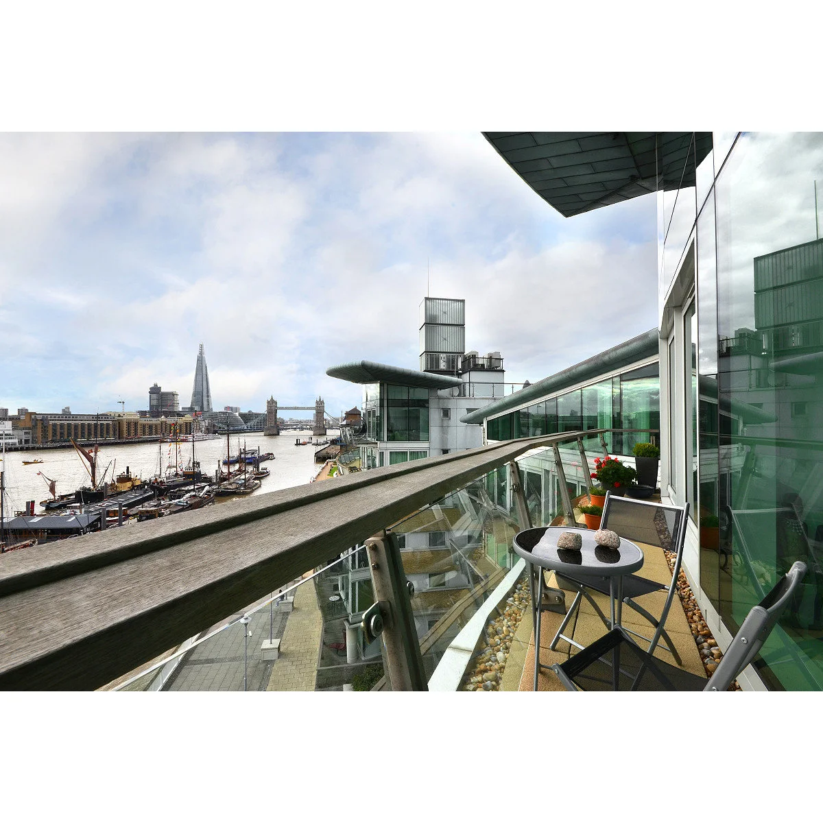 Very narrow apartment balcony with folding chairs and a small round table beside glazing