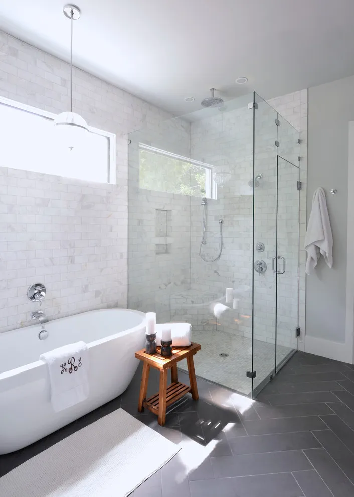 Dark rectangular tiles sit beneath a white freestanding bath and bright windows
