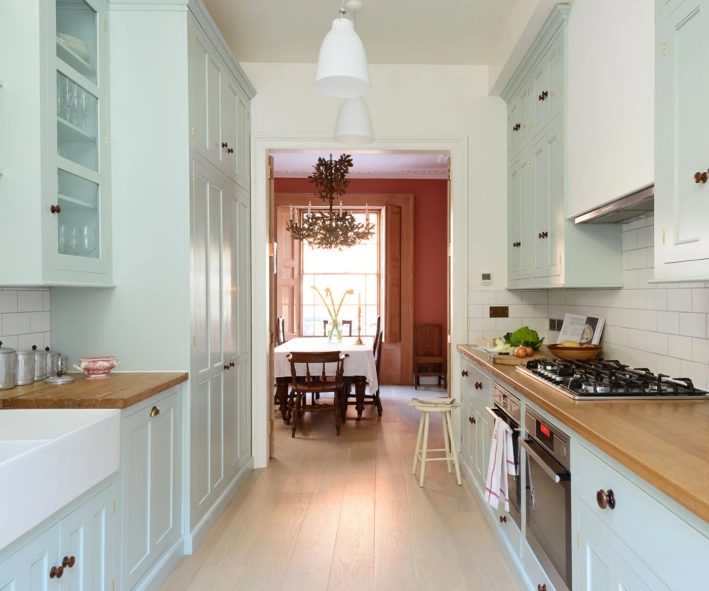 Light blue galley kitchen with wooden counters, tall cabinets and a dining room beyond