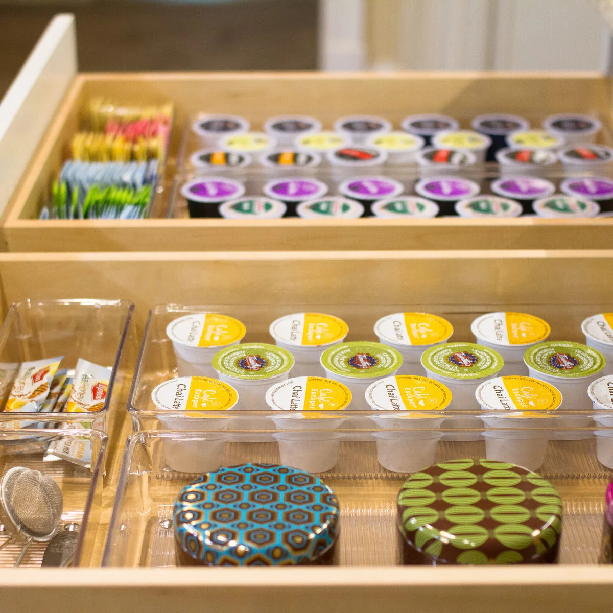 Open shallow drawers with coffee pods, tea packets and small accessories in clear organizers