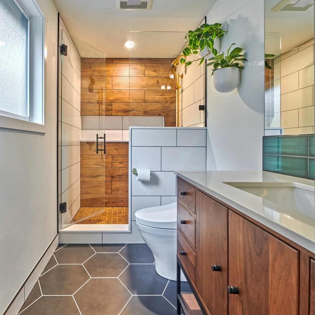 A wood-front vanity faces a compact shower with wood-look panels, white wall tiles and a dark hexagonal floor.