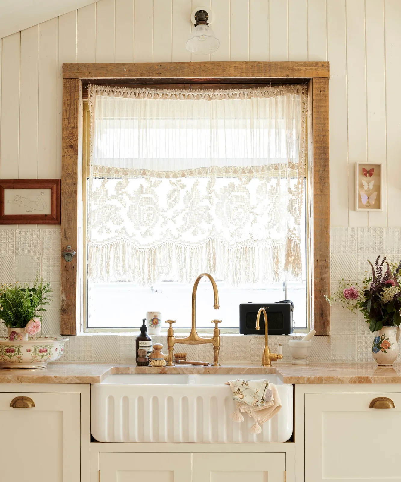 Short lace curtain at a wood-framed kitchen window above a cream sink area