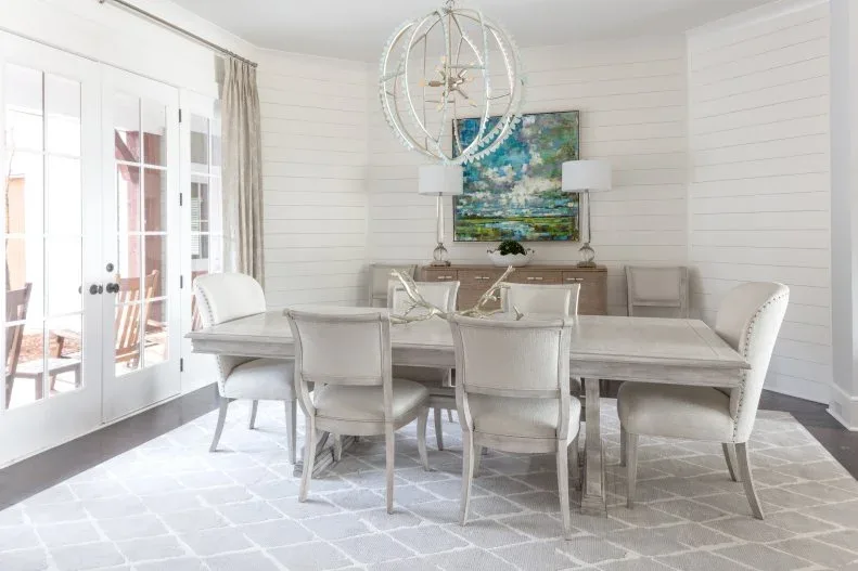 Light dining table with pale studded chairs, white horizontal wall boards and glass doors to a patio.
