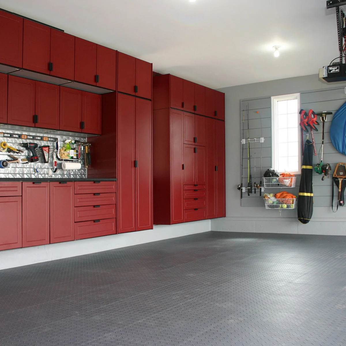 Garage with red workbench cabinets on one wall and fishing rods and sports equipment stored beside a window.