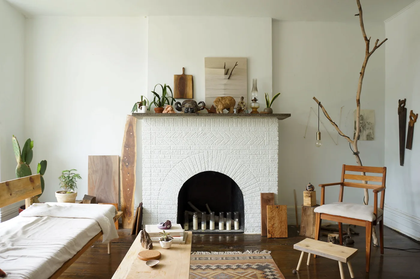 White brick arched fireplace with pale candles in a line inside the dark opening and wood pieces nearby.