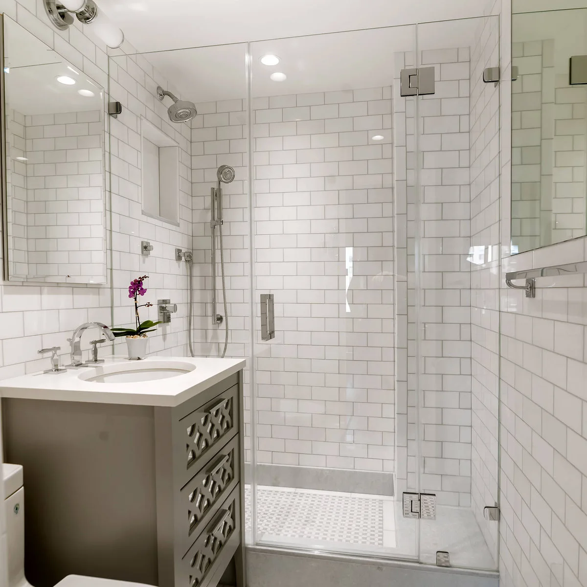 Narrow bathroom with white subway tiles, a compact grey vanity and clear glass shower door