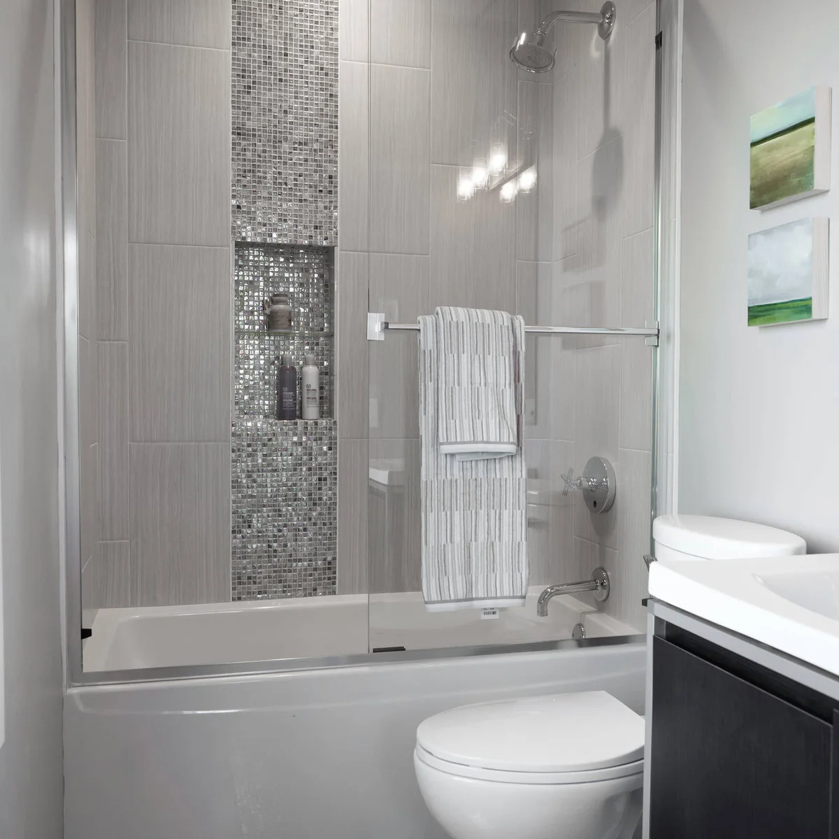 Compact tub shower with a vertical mosaic strip containing two shelves beside a glass screen