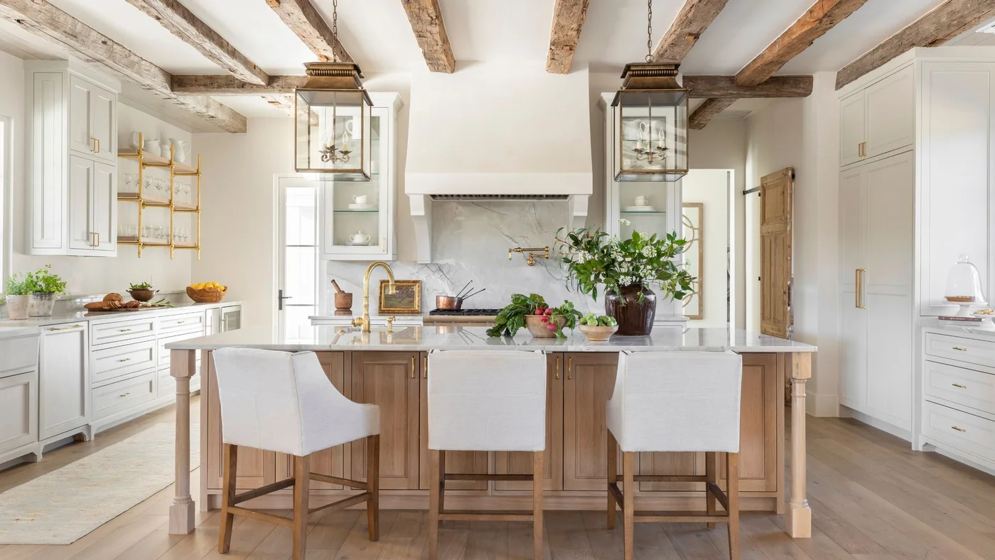 White framed cabinets surround a timber island beneath exposed beams and two large lantern pendants.
