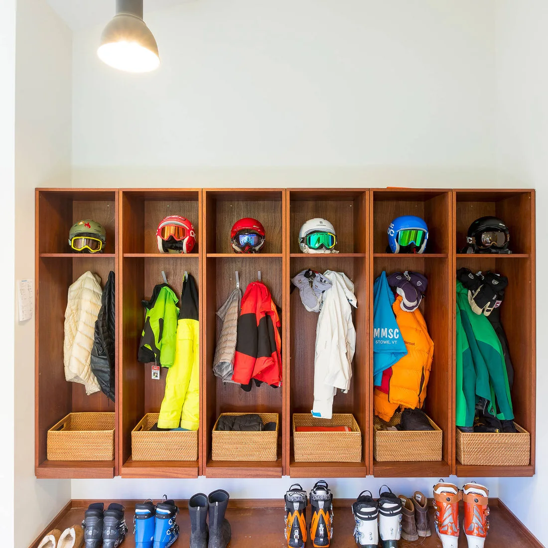 Wooden entry compartments with hanging outdoor clothing, helmets, baskets and boots below