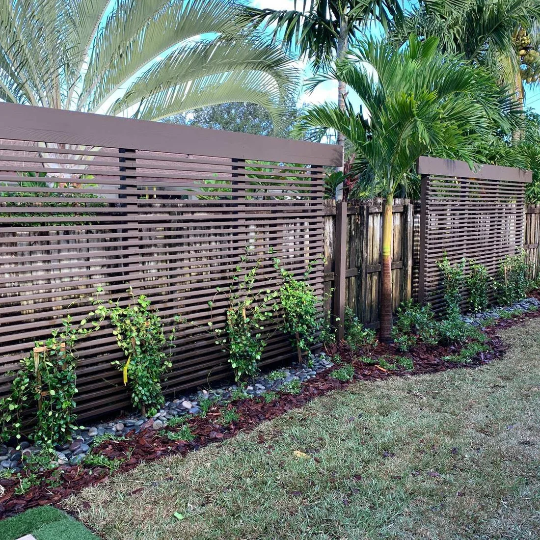 Two broad horizontal timber screens stand behind palms and climbing plants in a garden