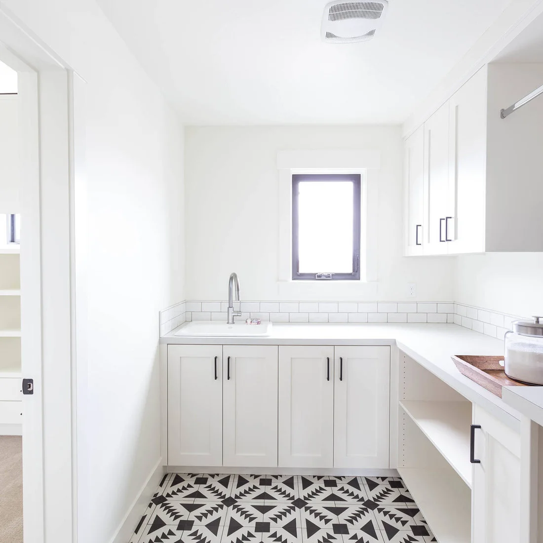 White cabinets and a U-shaped counter surround a utility sink beneath a window above a black-and-white graphic floor.