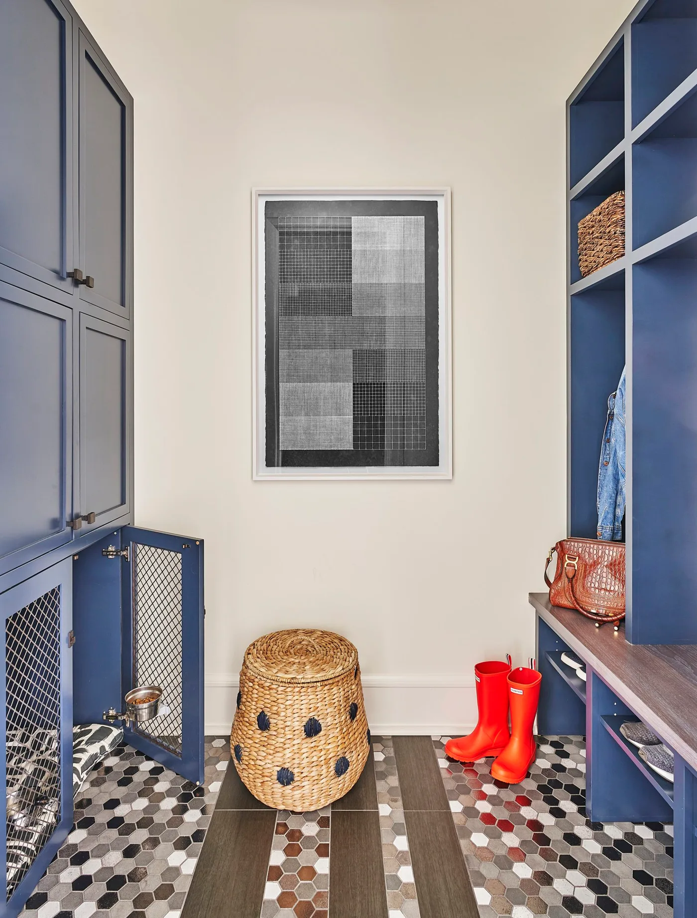 Blue mudroom with tall cabinets and a mesh-front pet compartment on one side, open cubbies and wooden bench opposite, patterned floor, and red boots.