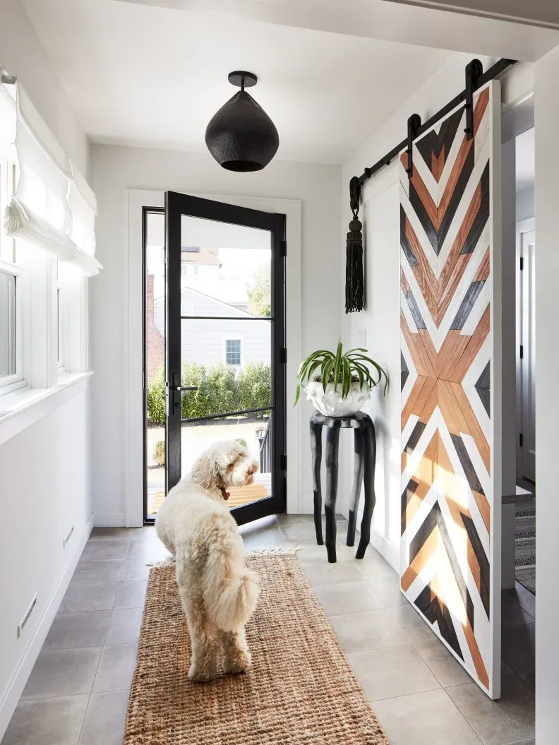 White entry with black glazed front door, geometric wood-patterned sliding barn door, small black table, plant and plain mat
