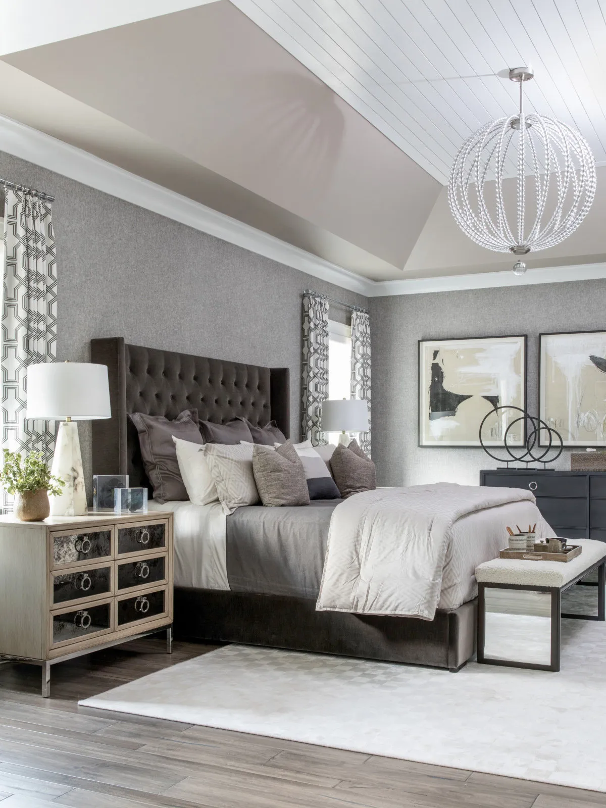 A tall dark upholstered headboard sits below a pale boarded ceiling in a gray bedroom.